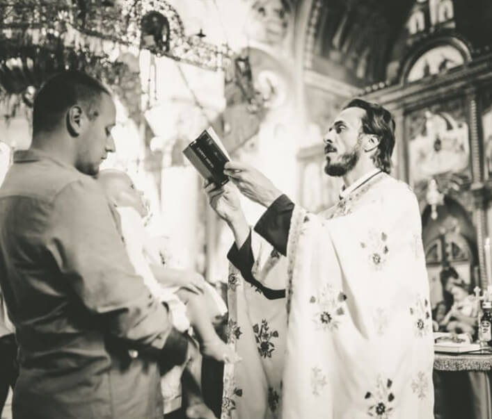 crno-bela slika na kojoj su beba koju otac drži u rukama i pop