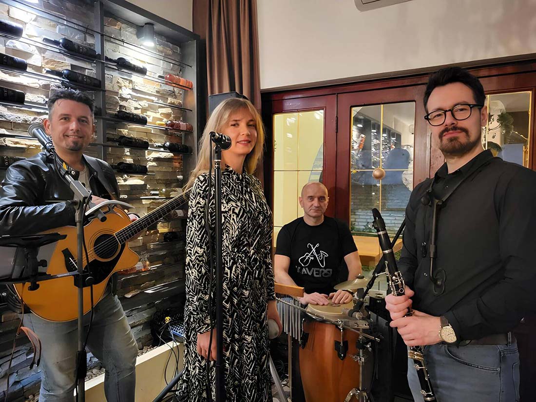 Akustični bend za proslave – muzičari sa gitarom, klarinetom, perkusijama i pevačicom tokom nastupa u restoranu.