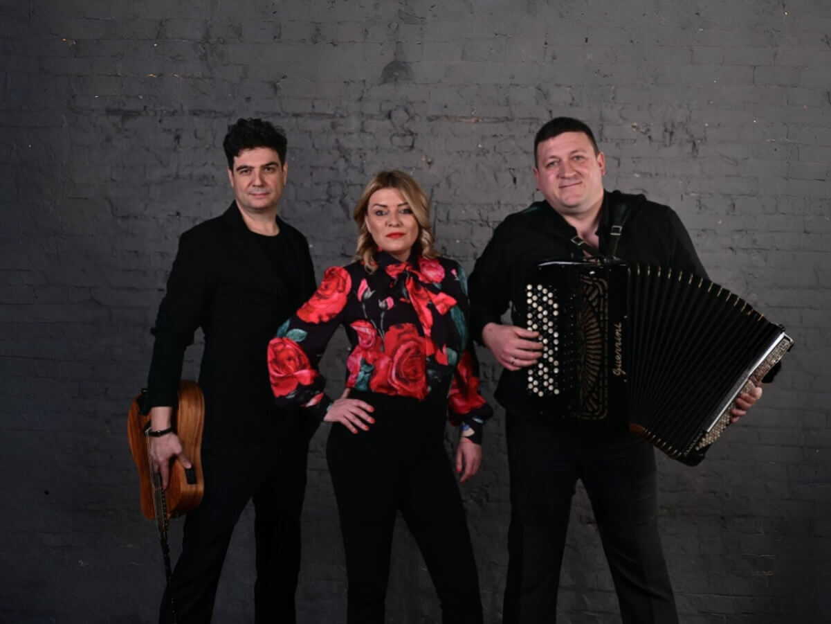 dva muškarca u crnom sa muzičkim instrumentima i žena u crvenoj košulji između njih