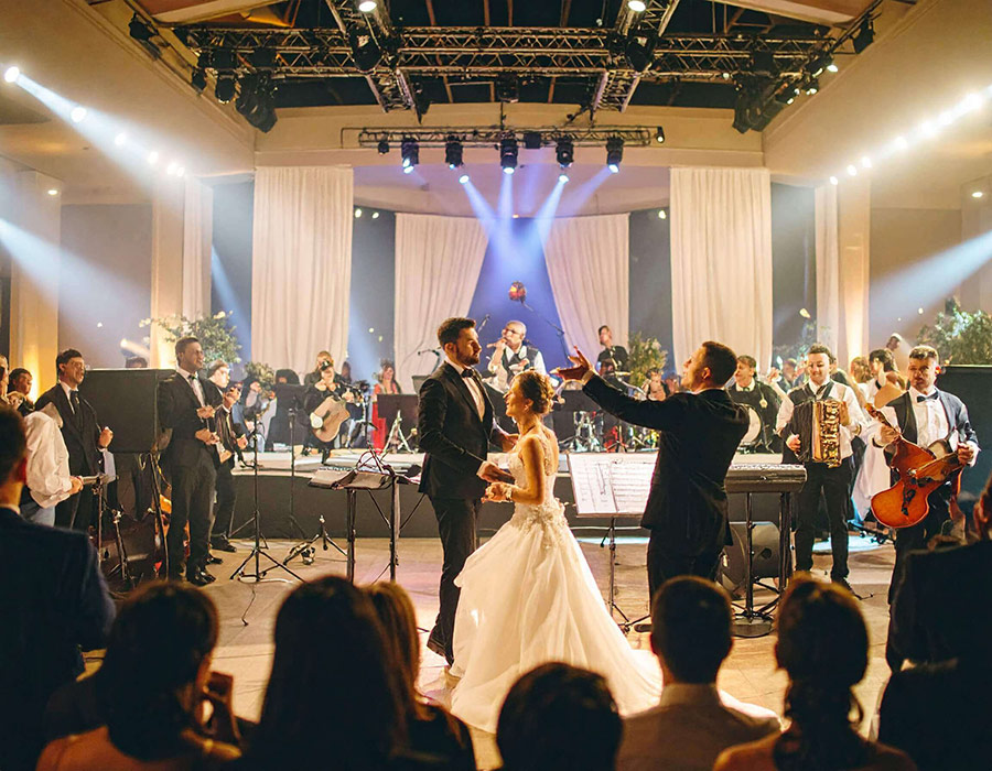 Mladenci plešu uz veliki svadbeni orkestar sa živom muzikom u luksuznoj sali u Srbiji.