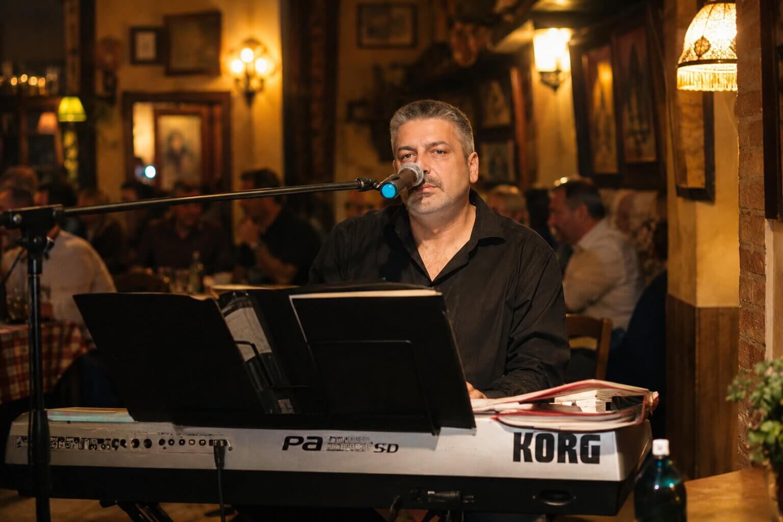 Bojan Mažestik svira Korg klavijaturu i peva tokom nastupa uživo pred publikom u restoranu sa tradicionalnim ambijentom.