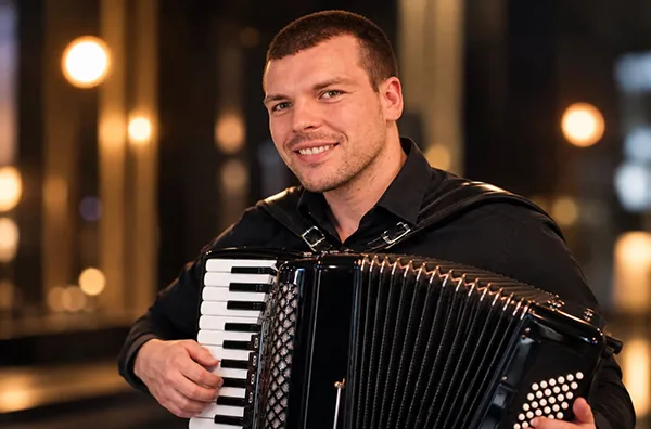 Slobodan Topić harmonikaš svira crnu harmoniku i osmehuje se, fotografisan u profesionalnom ambijentu sa zamućenom pozadinom.